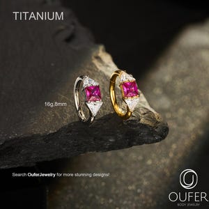 May include: Two titanium hoop earrings, one silver-toned and one gold-toned, each featuring a central square-cut pink gemstone flanked by two clear triangular stones. The text reads TITANIUM, 16g, 8mm, and OUFER BODY JEWELRY.