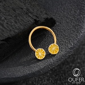 Könnte beinhalten: Ein goldfarbenes, kreisförmiges Hufeisen-Piercing mit zwei gelben Emaille-Anhängern in Form von Zitronenscheiben an den Enden. Der Text OUFER BODY JEWELRY ist in der unteren rechten Ecke des Bildes deutlich zu erkennen.