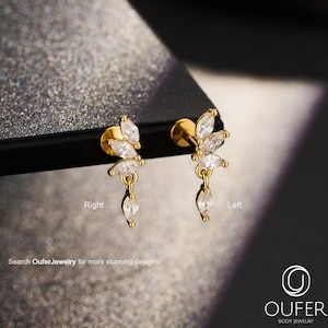 May include: Two gold-tone stud earrings featuring a cluster of marquise-cut clear stones arranged in a fan shape with a single dangling marquise-cut stone. The text Right and Left labels the earrings, and the logo OUFER BODY JEWELRY is visible.