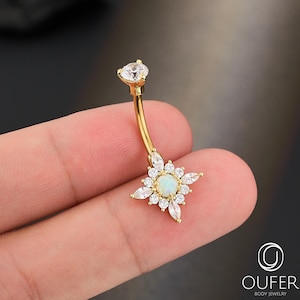 May include: A gold-tone curved barbell navel ring featuring a central round opal cabochon surrounded by a starburst arrangement of clear marquise and round-cut cubic zirconia stones, with a single round clear stone at the top end of the barbell.