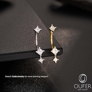 May include: Two curved belly button rings, one silver-toned and one gold-toned, each adorned with three square, clear gemstones. The jewelry is displayed on a dark surface. The text "Search OuferJewelry for more stunning designs!" is visible.
