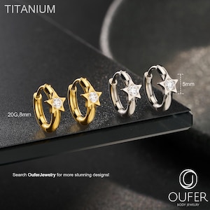 Puede incluir: Pendientes de aro de titanio dorados y plateados con colgantes en forma de estrella. Los pendientes se muestran en dos colores, con una gema transparente en el centro de cada estrella. El texto "TITANIUM" está en la parte superior de la imagen. Los pendientes tienen 8 mm de diámetro.