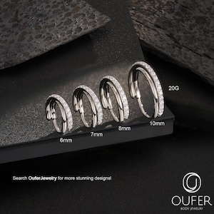 May include: Four silver hoop earrings with clear gemstones are displayed, ranging from 6mm to 10mm in size. The gauge is 20G. The text "Search OuferJewelry for more stunning designs!" is visible. The earrings are body jewelry.