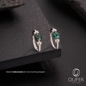 Puede incluir: Un par de pendientes de aro plateados con una cuenta verde moteada. Los pendientes se muestran sobre una superficie oscura. El texto dice "Search OuferJewelry for more stunning designs!"