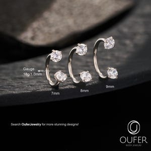 May include: Three silver body jewellery pieces with clear, round gemstones. The pieces are in a curved design, with one gemstone at each end. Sizes are 7mm, 8mm, and 9mm. The text says "Search OuferJewelry for more stunning designs!"