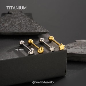 Puede incluir: Tres barras de lengua de titanio con diferentes diseños de extremos. Las barras son de calibre 14 y 16 mm de largo. Los extremos son un corazón, una estrella y una estrella. Las barras están sobre una superficie gris.  14g 16mm TITANIUM @outerbodyjewelry