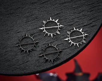 May include: Four silver and black nipple rings with a spiked sun design. The rings are on a black surface with a red background.