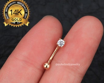 May include: 14k gold curved barbell with a clear round gemstone. The barbell is held in a hand.