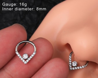 May include: A silver nose ring with a clear crystal in the center and a V-shaped design with clear crystals on each side. Gauge: 16g. Inner diameter: 8mm. @ouferbodyjewelry