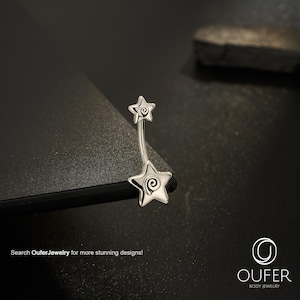 May include: A silver-toned curved barbell body jewelry piece featuring two star-shaped ends, each with a central spiral design. The text "Search OuferJewelry for more stunning designs!" and the "OUFER BODY JEWELRY" logo are visible in the image.