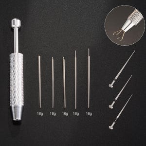 May include: A collection of silver piercing tools displayed on a black background. The set includes a textured handle, several straight needles marked 16g and 18g, and a small tool with grasping tips. These tools are for body piercing.