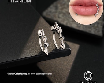 May include: Two silver titanium hoop earrings with cone-shaped spikes. The earrings are displayed on a dark surface. The word "TITANIUM" is at the top left. The image also includes a close-up of a person's lips with similar piercings. The text "Search OuferJewelry for more stunning designs!" is at the bottom.
