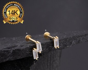 Puede incluir: Dos piezas de joyería corporal de oro con piedras rectangulares transparentes. La pieza de la izquierda tiene dos piedras, mientras que la pieza de la derecha tiene una piedra. La joyería está etiquetada como "A" y "B" respectivamente. La imagen también incluye un sello de oro con el texto "Best Quality 14K Gold Best Quality".
