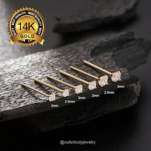 May include: Six gold nose rings with clear cubic zirconia stones. The stones are different sizes, ranging from 2mm to 3mm. The rings are laid out in a row from smallest to largest.