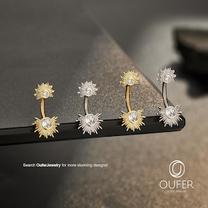 May include: Four curved barbell navel rings featuring sunburst-shaped ends with clear round crystals. Two rings are gold-toned and two are silver-toned. The text "Search OuferJewelry for more stunning designs!" and the "OUFER BODY JEWELRY" logo are visible.