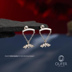 May include: A pair of silver-toned dangle earrings featuring a curved bar top connected by two delicate chains to a small bat-shaped charm. The text "Search OuferJewelry for more stunning designs!" and the "OUFER BODY JEWELRY" logo are visible.