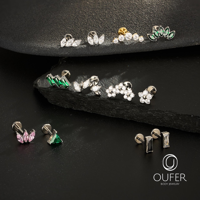 Puede incluir: Una colecci&oacute;n de joyas para el cuerpo, que incluye pendientes para orejas y cart&iacute;lagos. Los pendientes presentan varios dise&ntilde;os, como cristales transparentes con corte marquesa y redondos, gemas verdes y rosas, y un pendiente dorado con cristales transparentes.