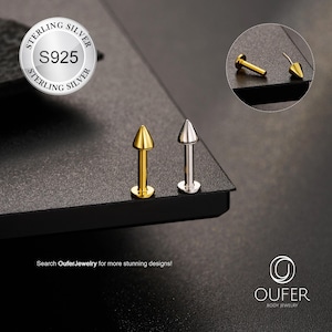 Puede incluir: Dos piercings labret, uno dorado y otro plateado, con una parte superior cónica y una base plana. Los piercings se muestran sobre una superficie oscura. La imagen incluye un recuadro circular que muestra un primer plano del piercing dorado. El texto dice "STERLING SILVER S925" y "OUFER BODY JEWELRY."