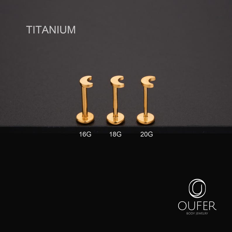 May include: Three gold-coloured titanium lip piercing studs in a crescent moon shape. The studs are labelled 16G, 18G, and 20G. The word "TITANIUM" is printed above the studs. The OUFER Body Jewelry logo is in the bottom right corner.