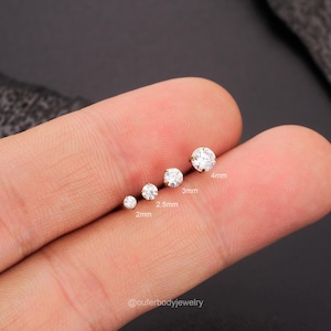 Może przedstawiać: Pięć przezroczystych, okrągłych kamieni szlachetnych o r&oacute;żnych rozmiarach na palcu. Kamienie szlachetne mają 2 mm, 2,5 mm, 3 mm i 4 mm. @outerbodyjewelry