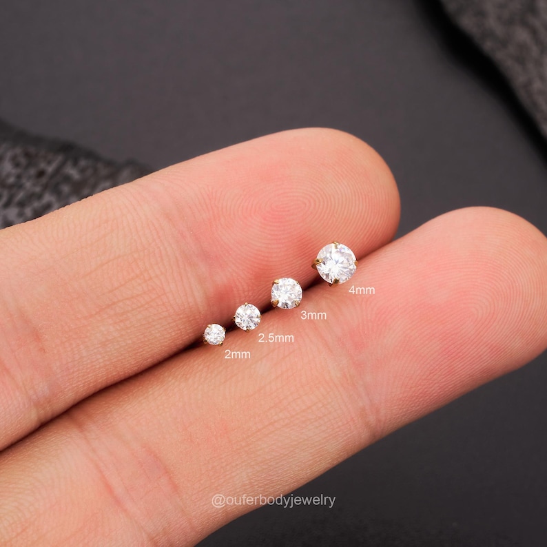 Może przedstawiać: Pięć przezroczystych, okrągłych kamieni szlachetnych o r&oacute;żnych rozmiarach na palcu. Kamienie szlachetne mają 2 mm, 2,5 mm, 3 mm i 4 mm. @outerbodyjewelry
