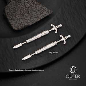 K&ouml;nnte beinhalten: Zwei silberfarbene, schwertf&ouml;rmige K&ouml;rperschmuckst&uuml;cke. Der Schmuck hat einen dekorativen Griff und eine Spitze. Der Text "14g 38mm" ist sichtbar. Das Bild enth&auml;lt auch den Text "Search OuferJewelry for more stunning designs!"