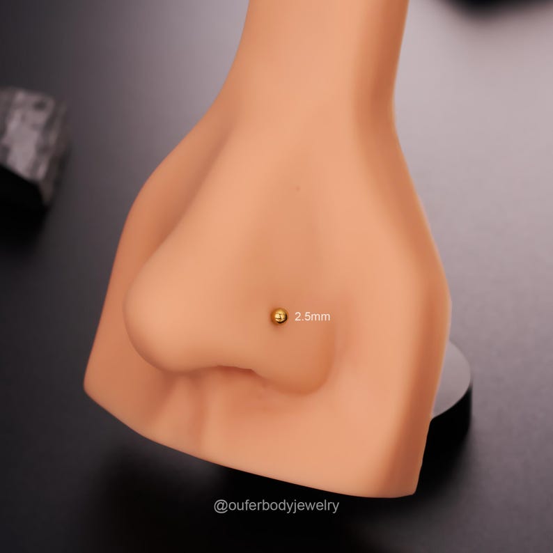 May include: A close-up of a gold nose ring with a 2.5mm ball on a mannequin. The text "@outerbodyjewelry" is visible at the bottom of the image.