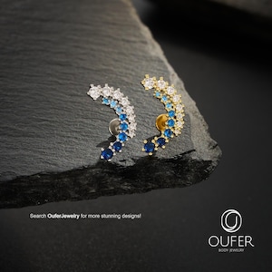 Könnte beinhalten: Zwei Ohrklemmen-Ohrringe mit geschwungenem Design. Einer ist silberfarben mit weißen und blauen Steinen, der andere goldfarben mit weißen und blauen Steinen. Die Ohrringe werden auf einer dunklen, strukturierten Oberfläche präsentiert. Der Text "Search OuferJewelry for more stunning designs!" ist sichtbar.