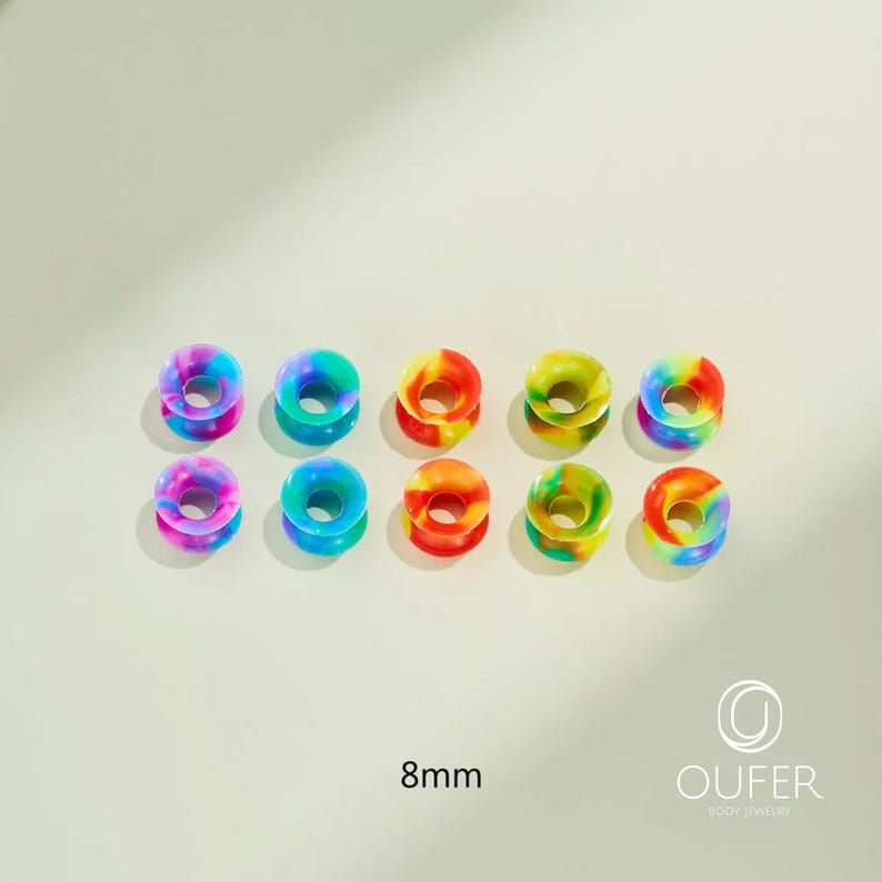 May include: Ten colorful 8mm (0.31 inch) ear gauges in a variety of rainbow hues. The gauges are donut-shaped, with a flared design. The image includes the text "8mm" and the brand name "OUFER BODY JEWELRY".