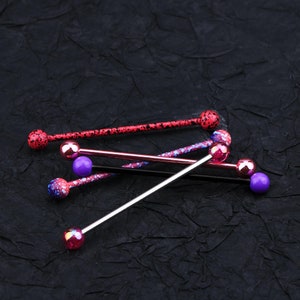 May include: Four different barbell style body jewelry pieces with colorful balls. The balls are pink, purple, and red with a speckled pattern. The barbells are made of metal.