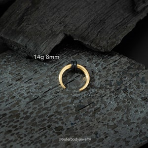 May include: Gold 14g 8mm horseshoe septum ring with black o-rings. The ring is on a black background.