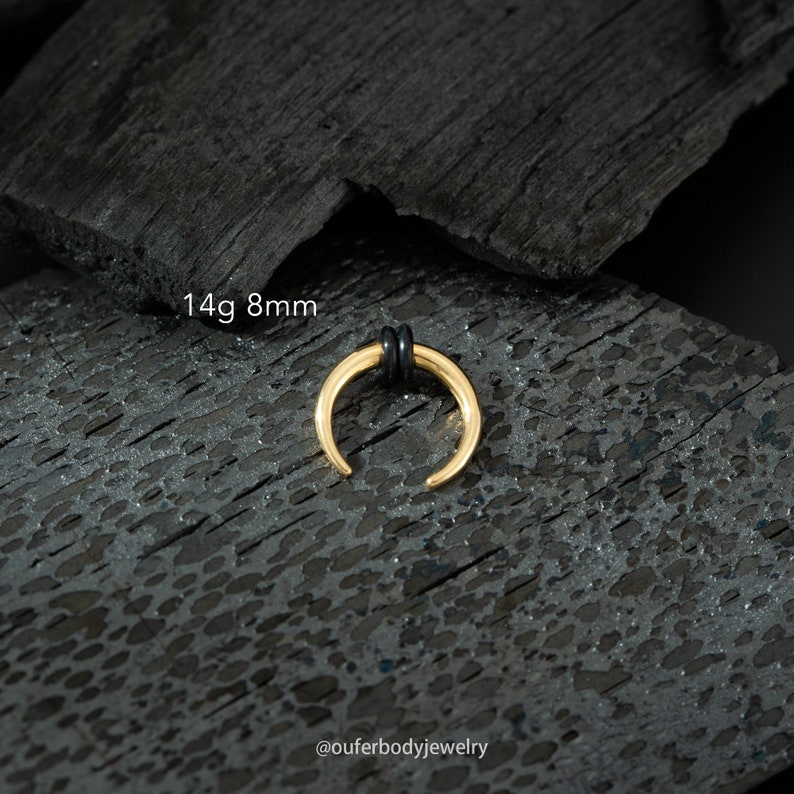 May include: Gold 14g 8mm horseshoe septum ring with black o-rings. The ring is on a black background.