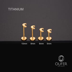 May include: Four gold-coloured titanium lip piercing studs in varying sizes. The studs are shaped like a crescent moon on a post, with sizes 10mm, 8mm, 6mm, and 5mm. The word "TITANIUM" is at the top of the image.