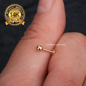 May include: A 14k gold nose stud with a small ball end. The stud is held in a hand, and the image includes the text "@ouferbodyjewelry".