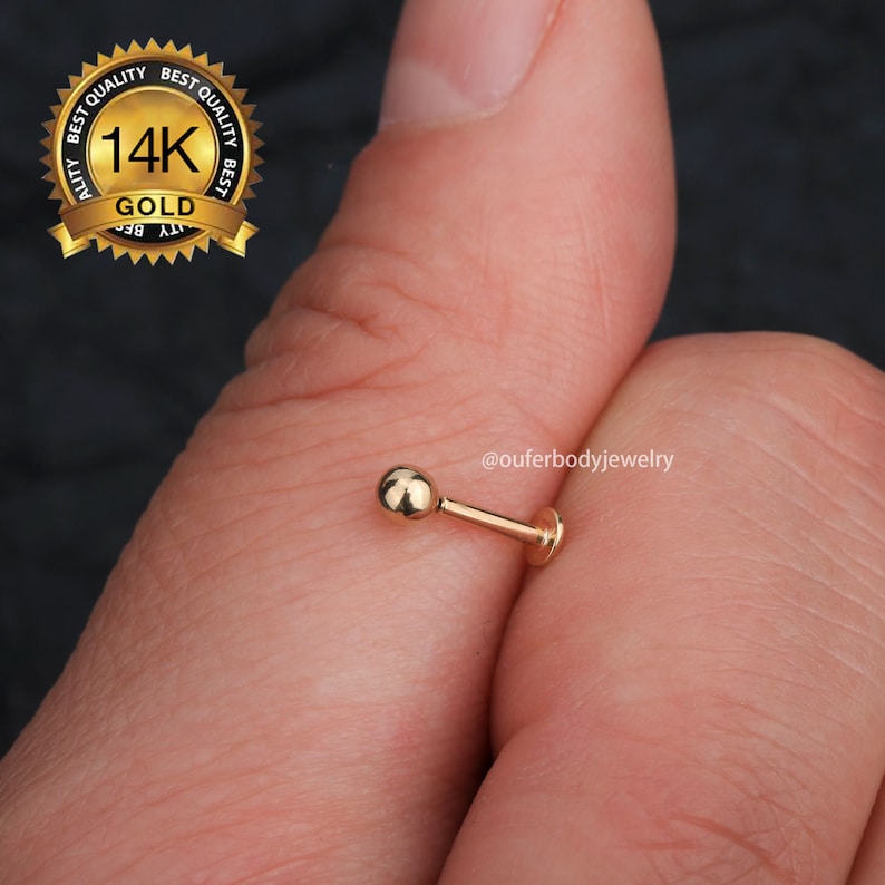 May include: A 14k gold nose stud with a small ball end. The stud is held in a hand, and the image includes the text "@ouferbodyjewelry".