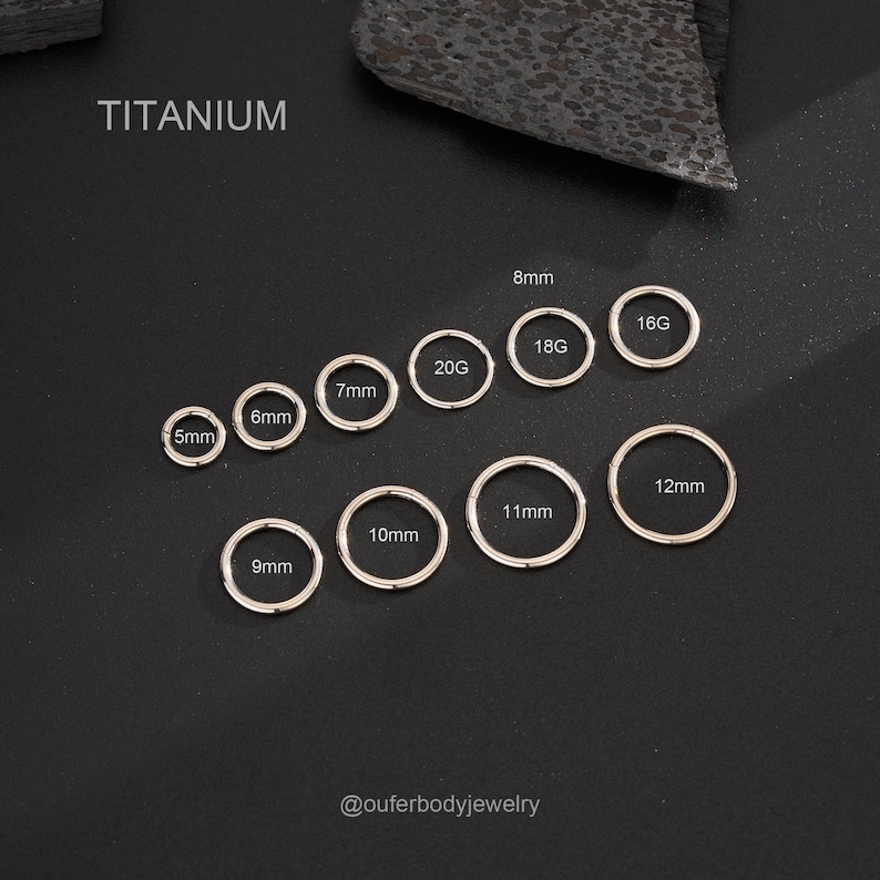 Puede incluir: Anillos sin costuras de titanio en varios tama&ntilde;os, de 5 mm a 12 mm, con las medidas etiquetadas en mil&iacute;metros. Los anillos est&aacute;n dispuestos en un semic&iacute;rculo sobre un fondo negro. El texto "TITANIUM" est&aacute; en la parte superior de la imagen, y el texto "@outerbodyjewelry" est&aacute; en la parte inferior.
