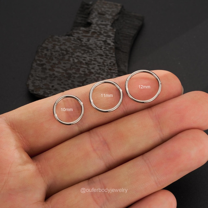 Puede incluir: Tres anillos de acero quir&uacute;rgico sin costuras de diferentes tama&ntilde;os, 10 mm, 11 mm y 12 mm, se muestran en la mano de una persona. Los anillos son ideales para piercings corporales.