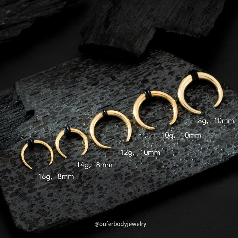 May include: A set of six gold horseshoe-shaped nose rings, ranging in size from 8 gauge and 10mm to 16 gauge and 8mm. The rings are displayed on a black wooden surface.