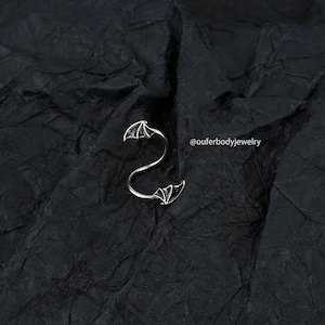 Peut inclure: Piercing d'h&eacute;lice en spirale argent&eacute; avec des accents d'ailes de chauve-souris. Le piercing est sur un fond noir. @ouferbodyjewelry
