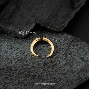 May include: Gold 10g 10mm septum ring with black o-rings. The ring is on a black textured surface.