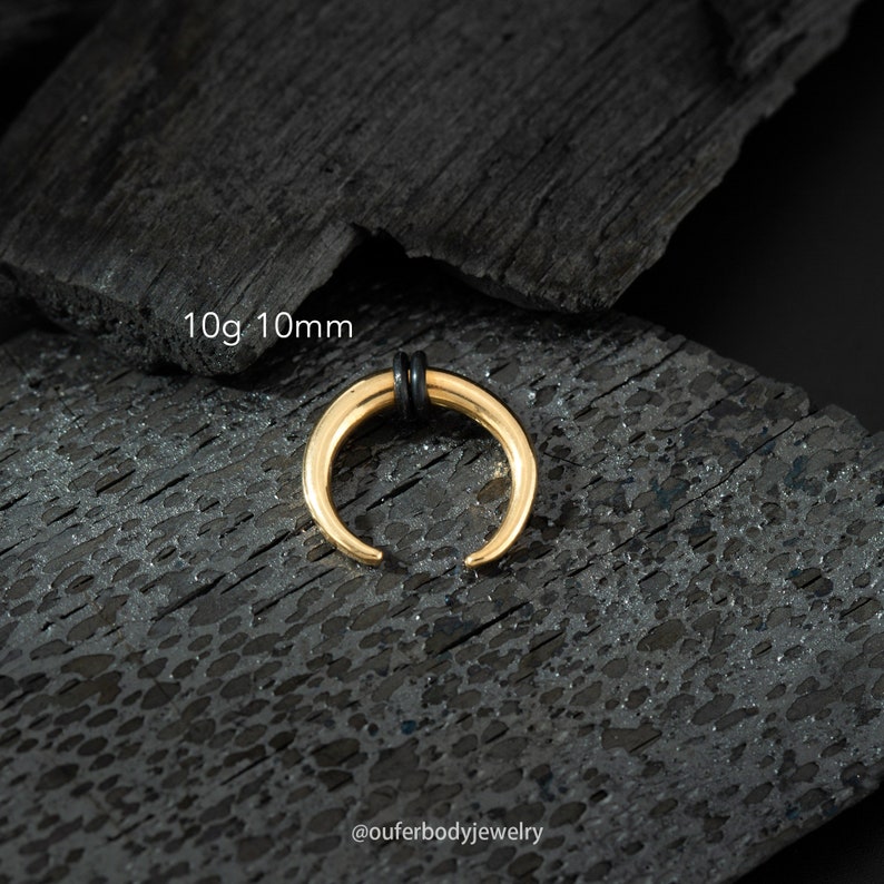 May include: Gold 10g 10mm septum ring with black o-rings. The ring is on a black textured surface.