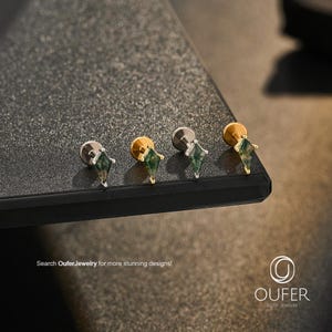 Puede incluir: Cuatro pendientes de botón con piedras de ágata musgosa verde en forma de cometa montadas en garras de metal. Dos pendientes tienen un acabado plateado y dos un acabado dorado. Cada pendiente incluye un cierre plano. Texto: Search OuferJewelry for more stunning designs!