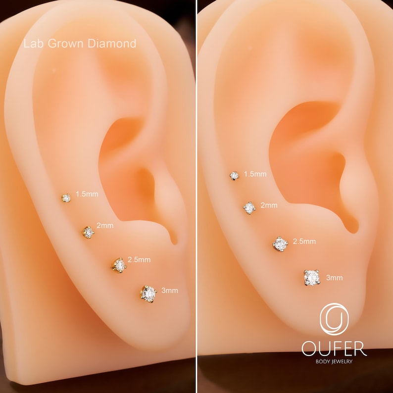 Puede incluir: Exhibici&oacute;n de pendientes de diamantes cultivados en laboratorio en varios tama&ntilde;os, incluyendo 1,5 mm, 2 mm, 2,5 mm y 3 mm. Los pendientes se muestran en un modelo de oreja bronceada, con etiquetas de tama&ntilde;o junto a cada uno. Tambi&eacute;n se ve la marca "OUFER BODY JEWELRY".