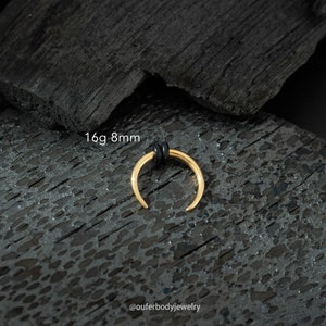 May include: Gold 16 gauge 8mm septum ring with a black rubber o-ring. The ring is on a black background.