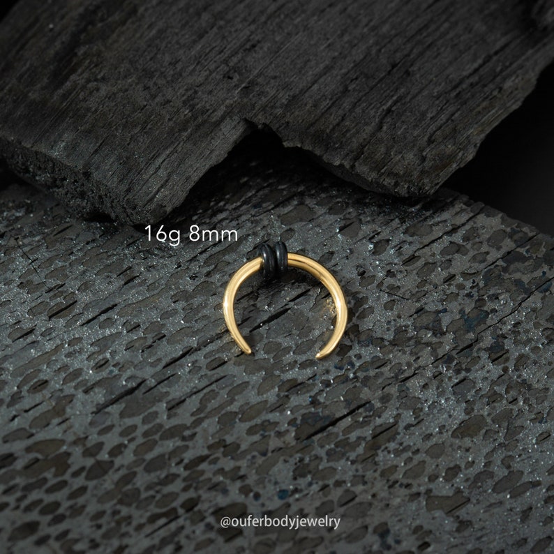 May include: Gold 16 gauge 8mm septum ring with a black rubber o-ring. The ring is on a black background.