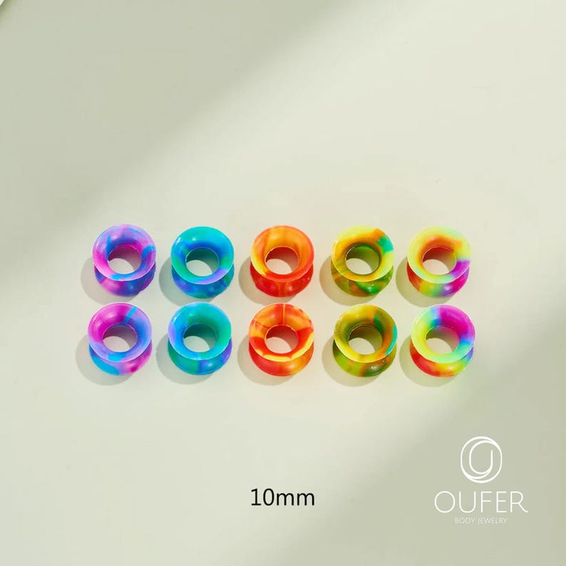 May include: Ten colorful, rainbow-swirled silicone ear gauges, each 10mm in diameter, are arranged in two rows of five. The gauges display a variety of vibrant colors, including blue, purple, orange, and green. The brand name "OUFER BODY JEWELRY" is visible.