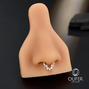 Op de afbeelding: Een zilveren septumring met een bladvorm, versierd met heldere edelstenen. De sieraden worden getoond op een neusmodel, waarbij de vorm en stijl worden benadrukt. Het merklogo "OUFER BODY JEWELRY" is zichtbaar.