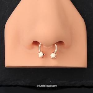 May include: Rose gold nose ring with star-shaped ends. The ring is shown on a model.