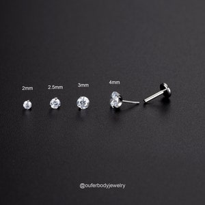 Puede incluir: Cuatro tama&ntilde;os de pendientes de bot&oacute;n de gema transparente en engastes plateados, que van de 2 mm a 4 mm. Los pendientes se muestran sobre un fondo negro. El texto "@ouferbodyjewelry" est&aacute; en la parte inferior de la imagen.
