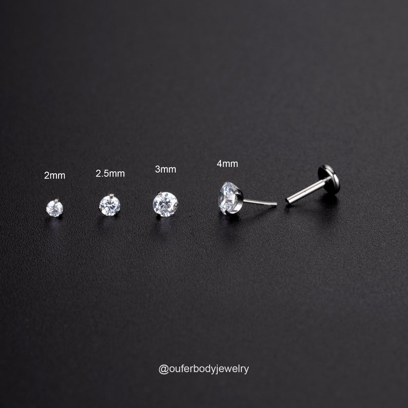 Puede incluir: Cuatro tama&ntilde;os de pendientes de bot&oacute;n de gema transparente en engastes plateados, que van de 2 mm a 4 mm. Los pendientes se muestran sobre un fondo negro. El texto "@ouferbodyjewelry" est&aacute; en la parte inferior de la imagen.